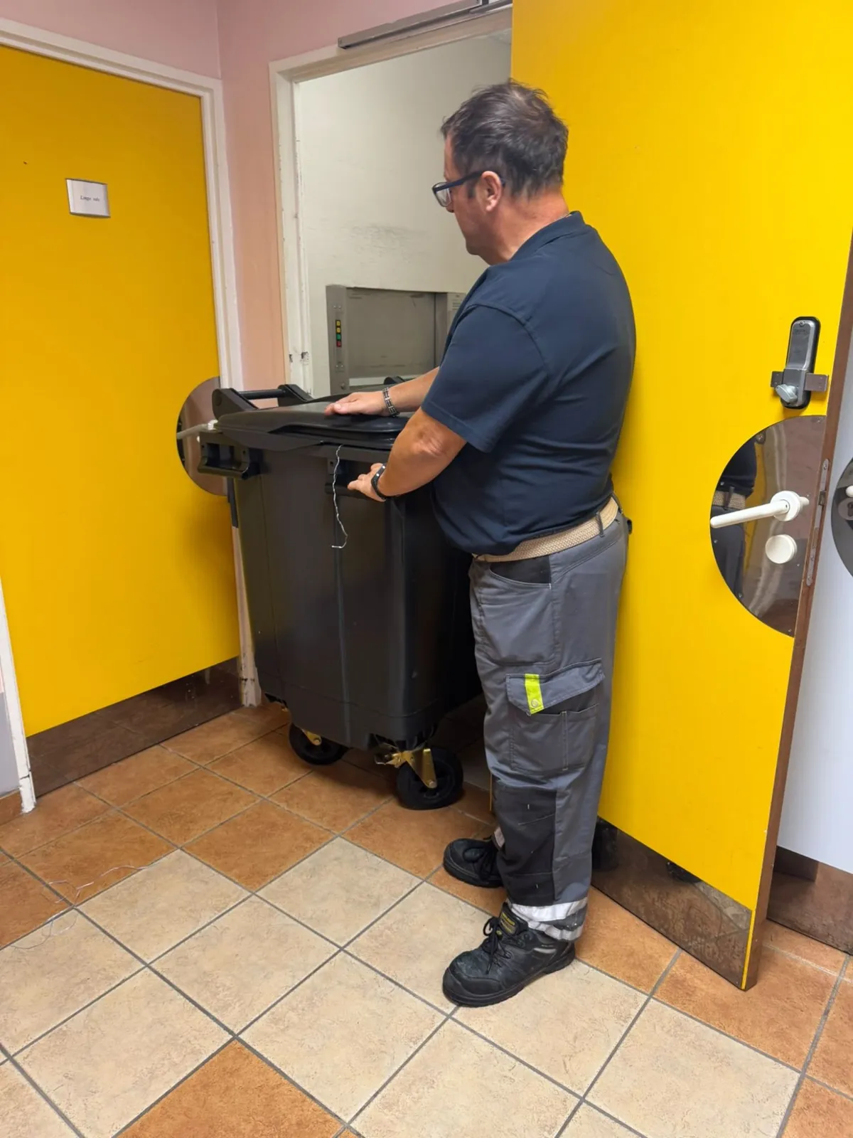 Agent de service déplaçant un conteneur de linge dans un établissement de santé
